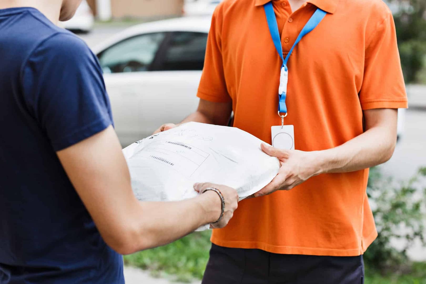 A person wearing an orange T-shirt and a name tag is delivering a parcel to a client. Friendly